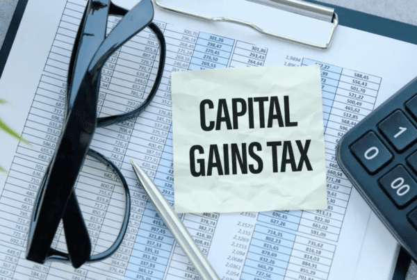 A pair of glasses, a pen, and a calculator lie on top of a financial document. A note with the text "CAPITAL GAINS TAX" is prominently placed on the document, highlighting the crucial work of business accountants in navigating these complex matters.