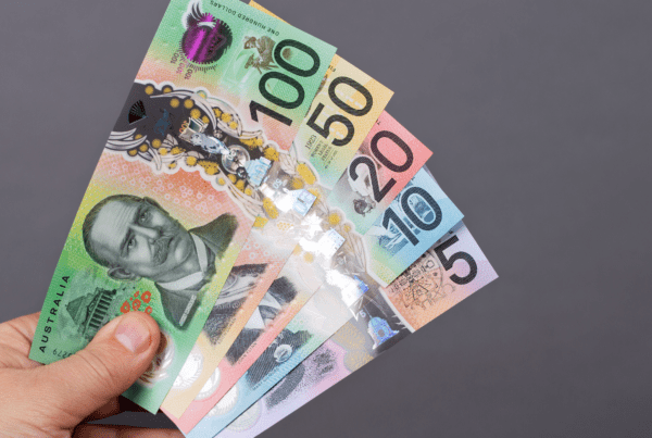 A hand holding Australian banknotes in denominations of 5, 10, 20, 50, and 100 dollars against a plain gray background. The colorful notes feature various designs and portraits. Perfect for business accountants seeking clarity or tax advice on handling such currency.
