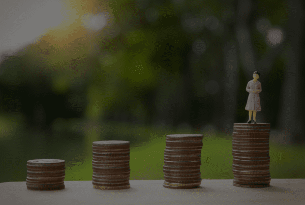 A small figurine of a person in a pink dress stands atop one of four progressively taller stacks of coins, symbolizing financial growth. Blurred greenery is seen in the background, representing the insightful guidance of business advisors.