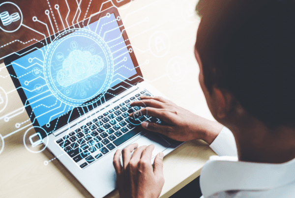 A person working on a laptop, with virtual icons and graphics related to cloud computing and digital connections overlayed on the image. The screen displays a cloud symbol surrounded by interconnected elements depicting data and technology concepts, ideal for business advisors seeking cutting-edge solutions.