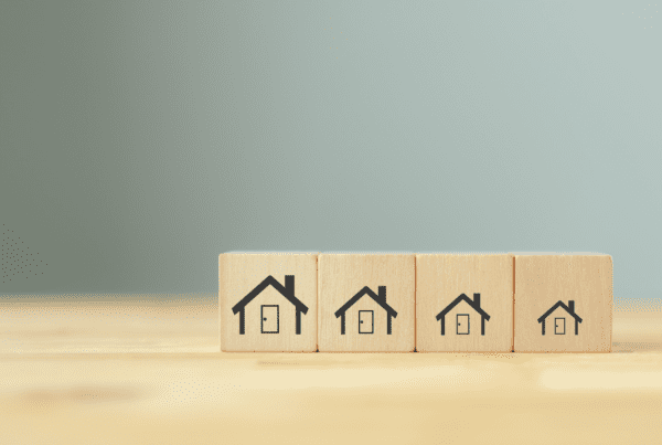 Four wooden blocks are lined up side by side on a wooden surface. Each block features a black house icon, with the houses decreasing in size from left to right. The background is a plain, muted light gray, symbolizing the detail-oriented approach of a Melbourne Accounting Firm offering precise tax advice.